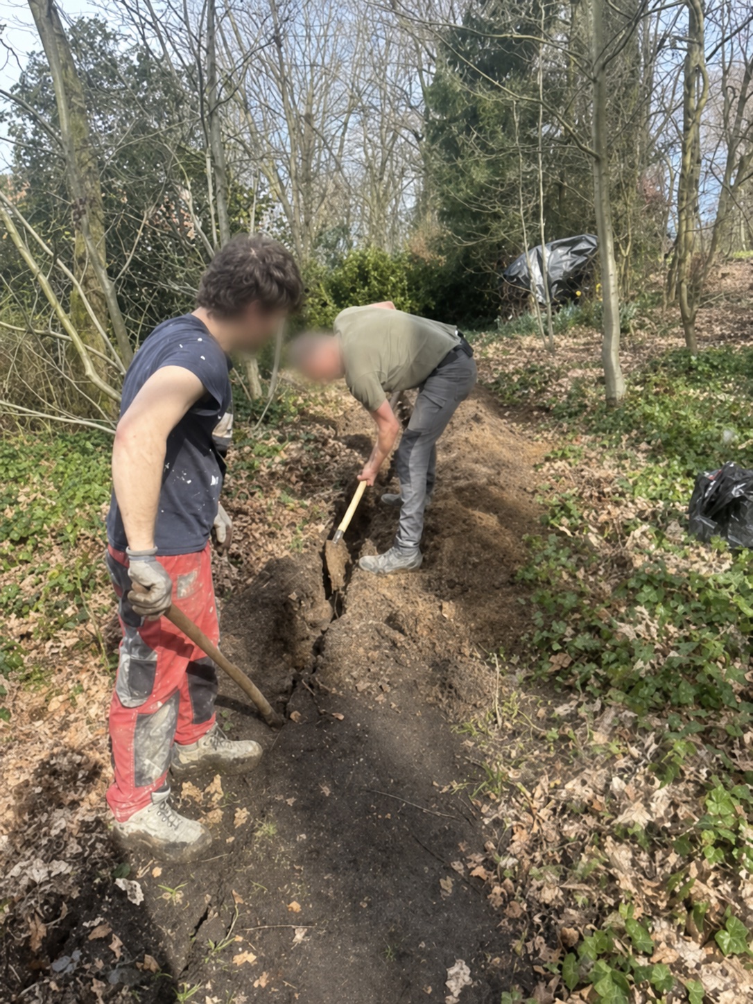 Deux ouvriers aux visages floutés réalisent une tranchée pour le passage de réseaux sur un chantier extérieur CharlElec